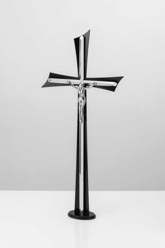 Krzyż stojący ze stali nierdzewnej z czarnym tłem i trójwymiarowym wizerunkiem Chrystusa w kolorze srebrnym.